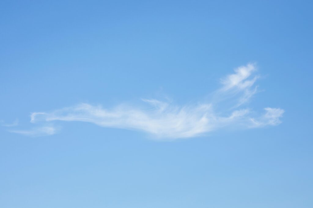 An artistic capture of a single wispy cloud in a vast blue sky, conveying tranquility.